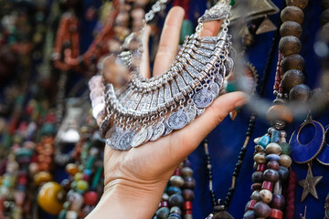 Hand of a female tourist holding a beautiful silver pendant of Moroccan costume jewelry in a store in Marrakech in Morocco, this city is full of street jewelry stores.