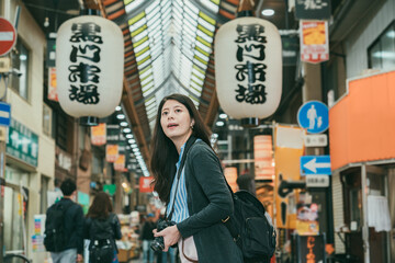 asian female tourist turning around and looking at the view in distance while visiting kuromon ichiba market in Osaka japan. translation on lantern kuromon ichiba market