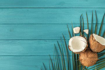 Coconut pieces with green palm leaves. Tropical fruit on the wooden turquoise background. Flat lay