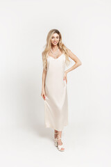Fashionable young elegance blonde woman with smile in stylish beige long dress with shoes walks on white background in studio. Party happy pretty girl