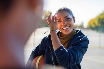 Young female smiles as she talks to her friend on a basketball court - Powered by Adobe