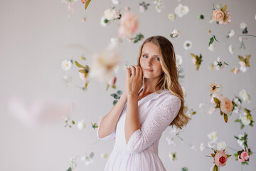 beautiful tender woman model stands on white background in a waterfall of flowers. Spring mood light atmosphere. Elegant girl on blooming background. Place for text. Banner for advertising. romantic