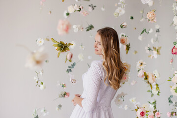 Obraz na płótnie Canvas beautiful tender woman model stands on white background in a waterfall of flowers. Spring mood light atmosphere. Elegant girl on blooming background. Place for text. Banner for advertising. romantic