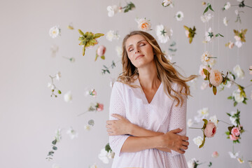 beautiful tender woman model stands on white background in a waterfall of flowers. Spring mood light atmosphere. Elegant girl on  blooming background dreams. Banner for advertising. romantic