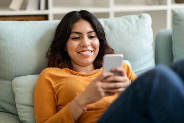 Smiling Young Arab Woman Messaging On Mobile Phone While Relaxing At Home