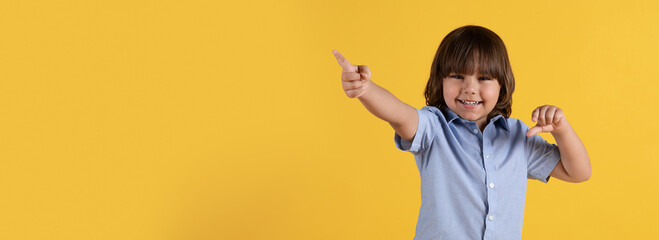 Great offer. Adorable little boy pointing aside and smiling, gesturing over orange background, panorama with empty space