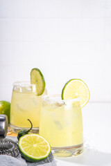 Boozy classic tequila  margarita refreshing alcoholic sweet and sour cocktail, with lime,  tequila, green chili pepper. With bar accessories, shaker, ice cubes on white table