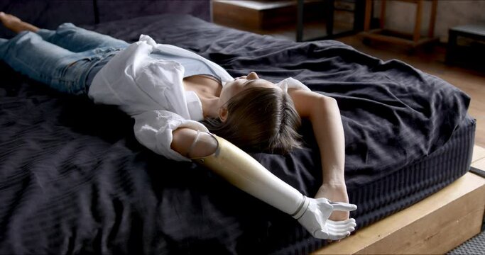 Lasy morning portrait smiling happy woman with prosthetic arm on black bed stretching, Lying on bed at home, girl with disability artificial prosthetic limb
