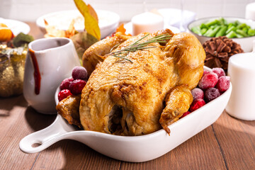 Thanksgiving family party dinner table setting with plates, cutlery, glasses, traditional dishes - baked turkey or chicken, pumpkin pie, fruits, mashed potatoes, green beans, wooden background