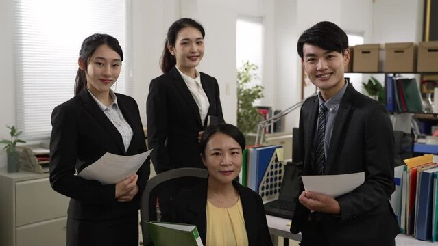 portrait of four professional asian businesspeople wearing suit posing in the office. they look at the camera with a confident smile with document in hands