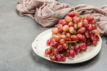 Trendy plate with a bunch of pink grapes. Vintage textile napkin, stone concrete background