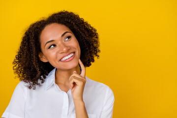 Portrait of cheerful pretty girl hand arm finger touch chin interested empty space isolated on yellow color background