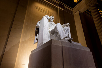 The Abraham Lincoln statue, sculpted by Daniel Chester French and carved by the Piccirilli Brothers, within the Lincoln Memorial in Washington, D.C. at night. Low angle wide shot.