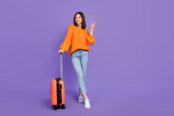 Full size photo of pretty young girl show v-sign baggage business trip wear trendy orange knitwear look isolated on violet color background