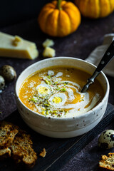Homemade pumpkin cream soup with quail eggs, parmesan , sour cream and pistachios and biscotti with dried tomatoes and pistachios on dark background .