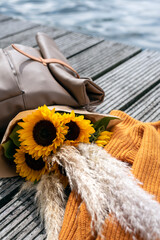 Traveler's backpack, diary, and a bunch of sunflowers lie on a pier.