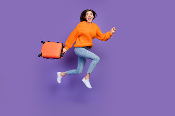 Full body photo of charming young girl carry travel suitcase run fast wear trendy orange knitwear look isolated on violet color background