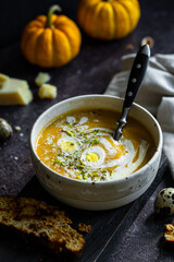 Homemade pumpkin cream soup with quail eggs, parmesan , sour cream and pistachios and biscotti with dried tomatoes and pistachios on dark background .
