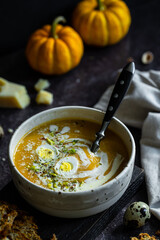 Homemade pumpkin cream soup with quail eggs, parmesan , sour cream and pistachios and biscotti with dried tomatoes and pistachios on dark background .