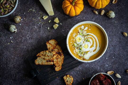 Homemade pumpkin cream soup with quail eggs, parmesan , sour cream and pistachios and biscotti with dried tomatoes and pistachios on dark background .