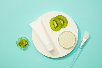 A fresh kiwi mask jar, a few thin slices of kiwi, and a tube of ice cream are shown on a white podium. The palm tree and the kiwi for the garnish