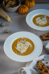 Homemade pumpkin cream soup with quail eggs, parmesan , sour cream and pistachios and biscotti with dried tomatoes and pistachios on white background 