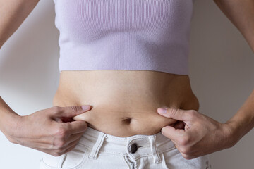 Cropped image of overweight woman, tucking, hiding fat naked big excessive belly with navel in white jeans. Dangling down stomach, big size tummy. Drag away of abdomen. Go on diet, liposuction