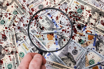 A hand with a magnifying glass against the background of scattered American dollar bills with blood drops, close-up. Flat lay. The concept of counterfeit money, bribery and illegal corruption