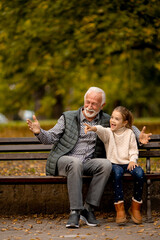 Grandfather spending time with his granddaughter on bench in park on autumn day