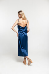 Fashionable trendy beautiful woman model blonde in blue stylish blue long open back dress with shoes walks and poses on a white background in studio