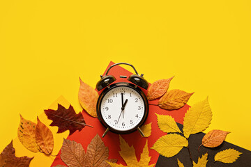 Daylight saving day. Fall Back. Black Alarm clock and autumn leaves on yellow background. Daylight...