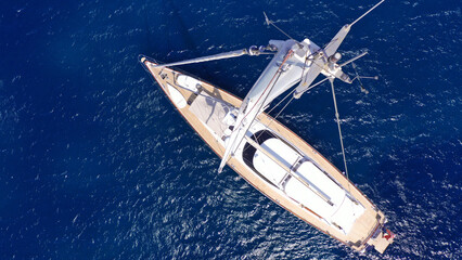 Fototapeta premium Aerial drone top down photo as seen from top of mast of beautiful sail boat with wooden deck anchored in deep blue Aegean sea