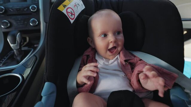 Close-up footage of happy cute baby boy sitting in children's car seat. Safe transportation of toddler in auto. Emotion, expression. Comfortable transportation. Safety and security