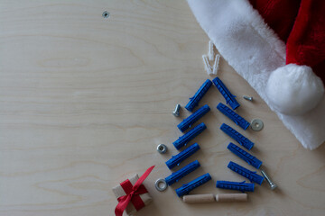Santa`a hat. Christmas tree shape with dowels, nuts, screws and gift on a plywood background, Cope space, top view