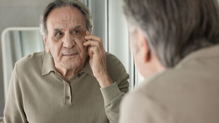 Old man looks at the wrinkles around the eyes in the mirror	
