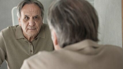 Old man looking at his face in the mirror	