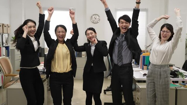 portrait of overjoyed business team jumping up and waving raised arms while looking at camera cheering for exciting good news in the office