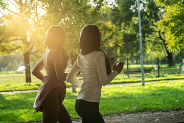 Two young Muslim females covered with Islamic hijab jogging at the city street.