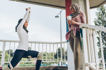 Two young Muslim females covered with Islamic hijab jogging at the city street.They're stretching under city overpass