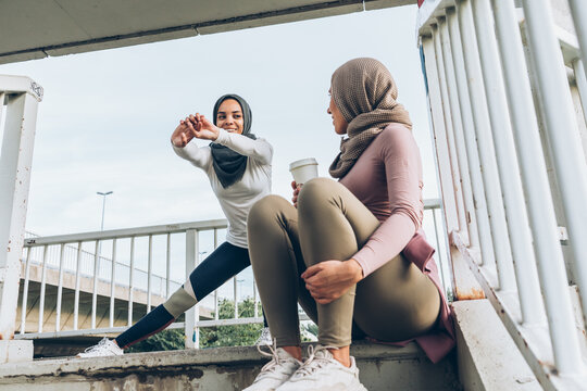 Two young Muslim females covered with Islamic hijab jogging at the city street.They're stretching under city overpass - Powered by Adobe
