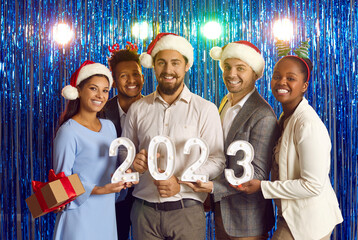 Team of happy smiling diverse multiracial male and female employees in Santa caps standing on...