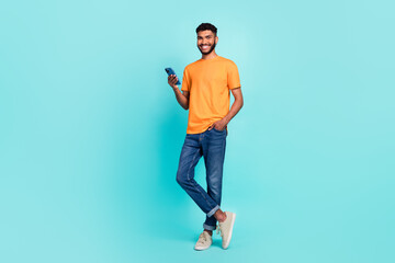 Full length photo of good funny pretty guy wear orange t-shirt communicating modern gadget empty space isolated teal color background