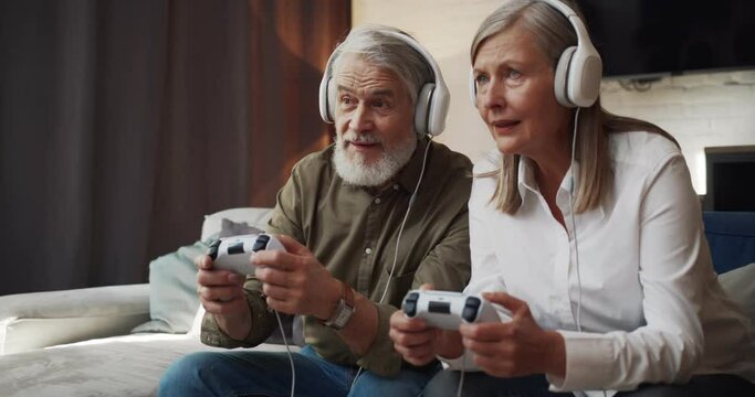 Mature couple in headphones competiting in video games at home