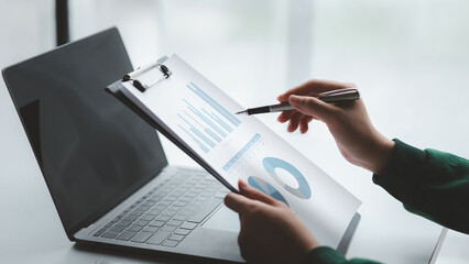 A close-up view of a businessman pointing at a bar chart on a company financial document prepared...