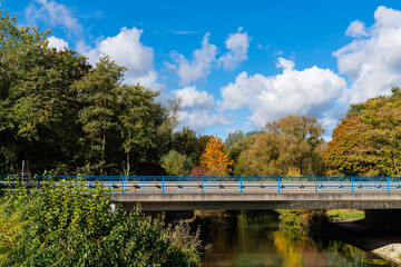 Autumn landscape with a concrete bridge over a river and a blue sky with white clouds.
