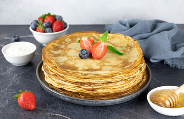 French crepes, thin pancakes with berries on a gray marble background. Pancakes with berries. A stack of pancakes with strawberries, blueberries, honey, sour cream. Russian blini. Maslenitsa.