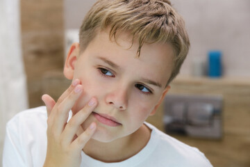 The teenager looks at the skin of his face in annoyance.