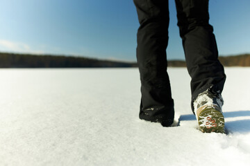 No face photo. Picture of legs in black warm clothes and green shoes walking in snow drift on white...