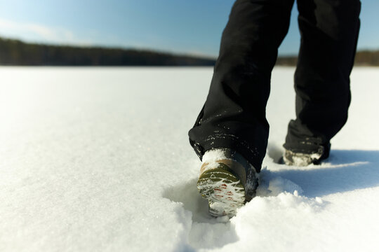No face. Outdoor image of feet and legs in winter active wear and shoes stepping in snowy field with forest on background, walking in snow draft on sunny frosty cold day with blue clear sky