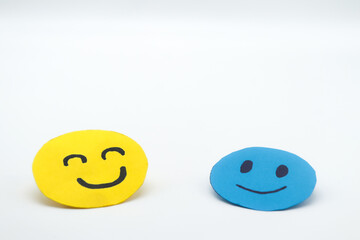 two happy smiling faces, made of blue and yellow paper cut out on a white background. Concept of well-being, happiness, companionship, kindness